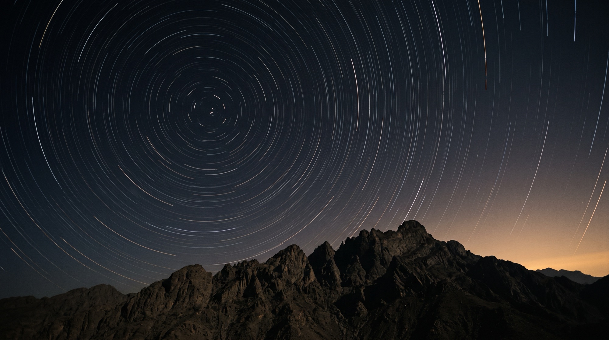 Star trails circling over a ridge of the Hajar mountains at night, first light on the horizon